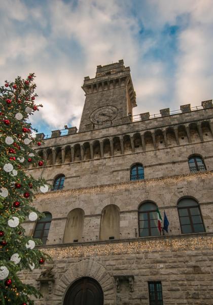 Geschmückter Weihnachtsbaum vor einem historischen Gebäude mit Turm und Uhr.