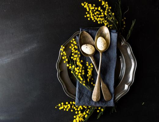 Uova di quaglia su cucchiai con fiori gialli e piatto decorativo.