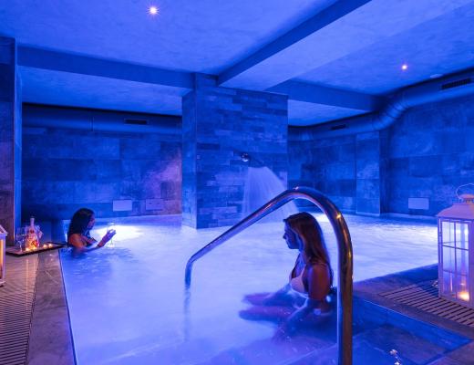 Piscina termale con luci blu e candele, atmosfera rilassante.