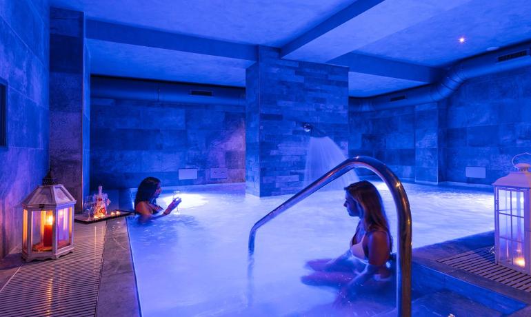 Piscina termale con luci blu e candele, atmosfera rilassante.